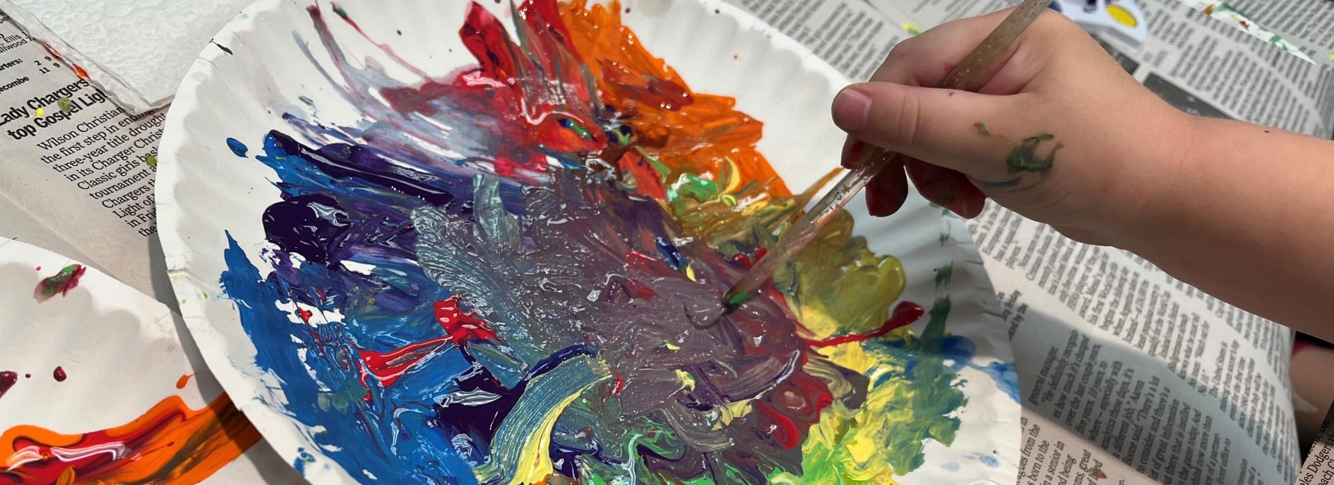 Picture of a child's hand holding a paintbrush and spreading multicolor paint